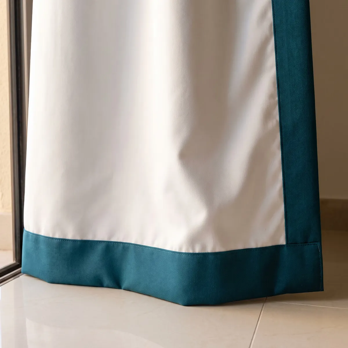 Back of a curtain, white lining running into a teal border at the side and bottom hem, beside a sliding door