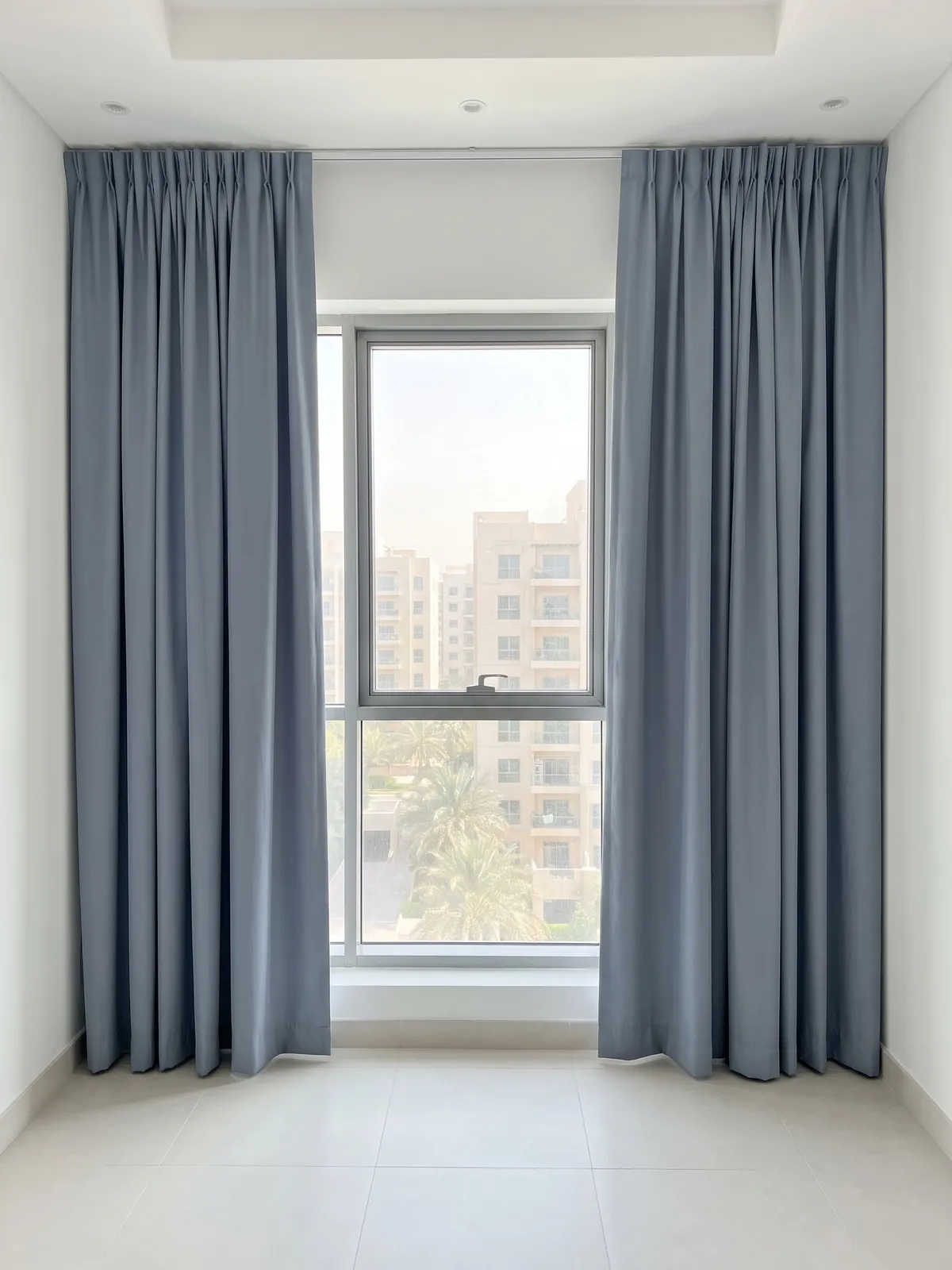 Dusty blue lined curtains drawn open at both sides of a tall window, their hems reaching the floor, apartment blocks outside