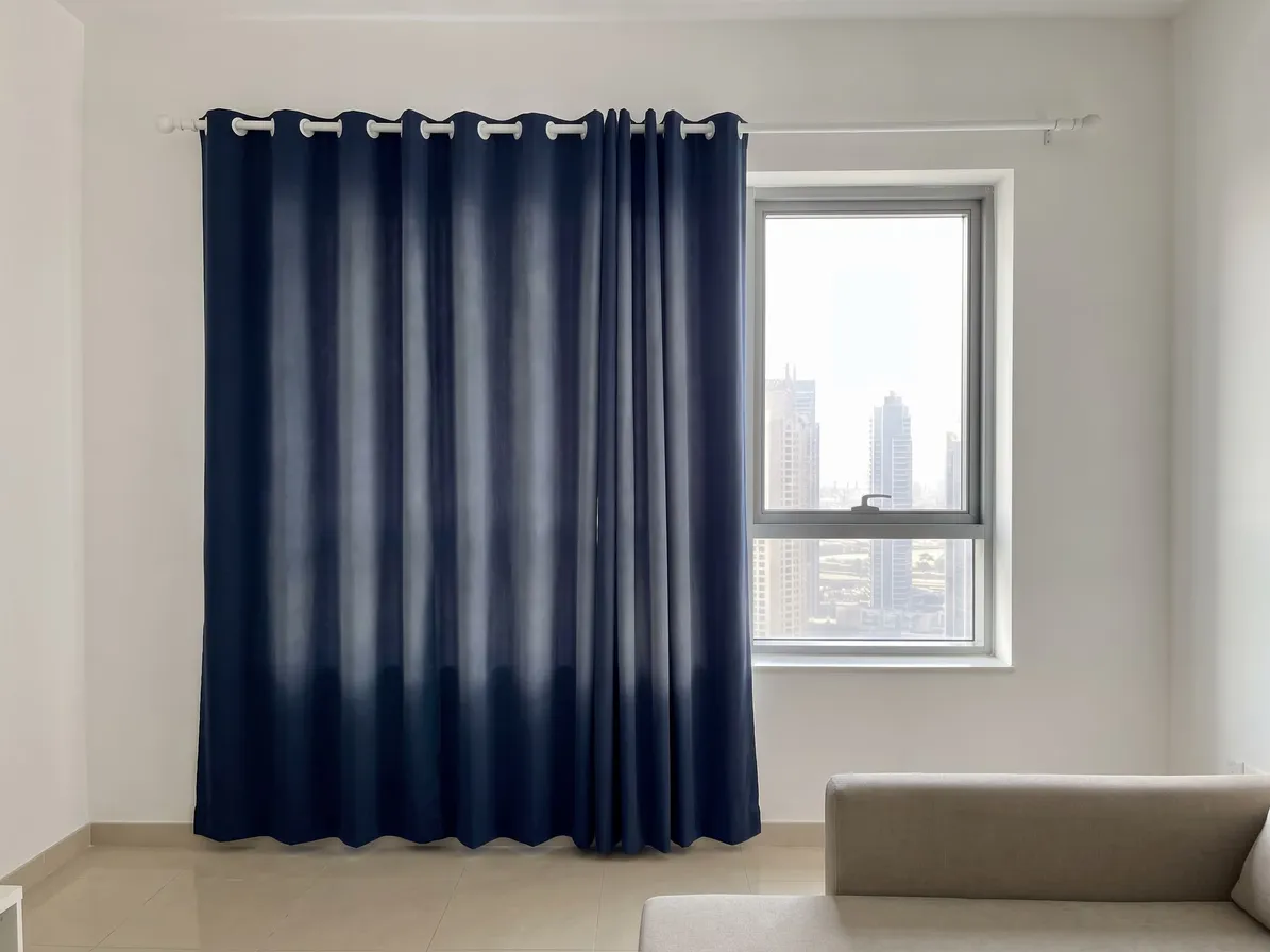 Navy eyelet curtain with pale faded streaks down its folds, hanging beside a window with towers, a beige sofa at the lower right