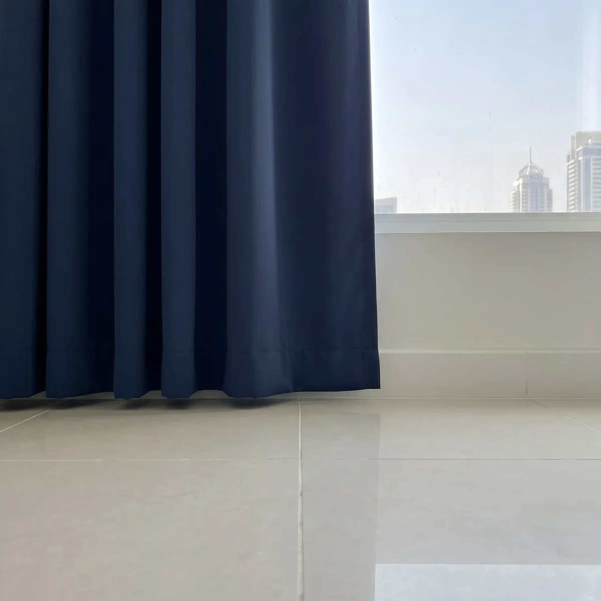 Navy curtain hem hanging just clear of a pale tiled floor, seen at floor level, a window with towers at the right