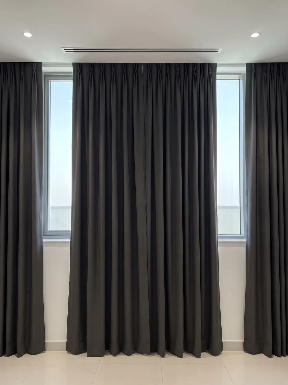 Charcoal curtains closed under a ceiling cove that ends at the glass, thin bands of daylight showing down both sides of them