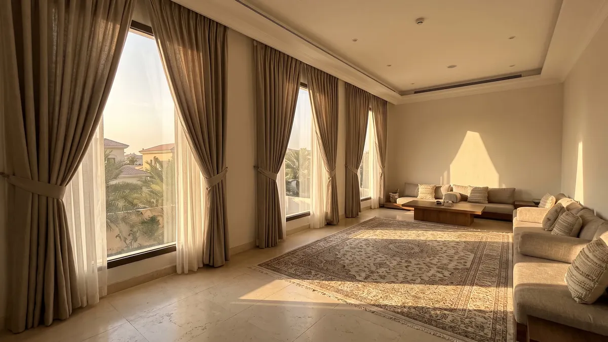 Taupe curtains tied back over ivory sheers on tall windows in a villa majlis with low seating