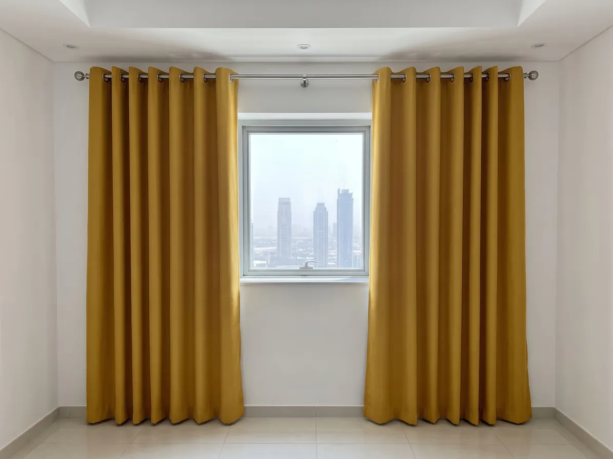 Mustard-yellow eyelet curtains on a steel pole, drawn open either side of a small square window with towers outside