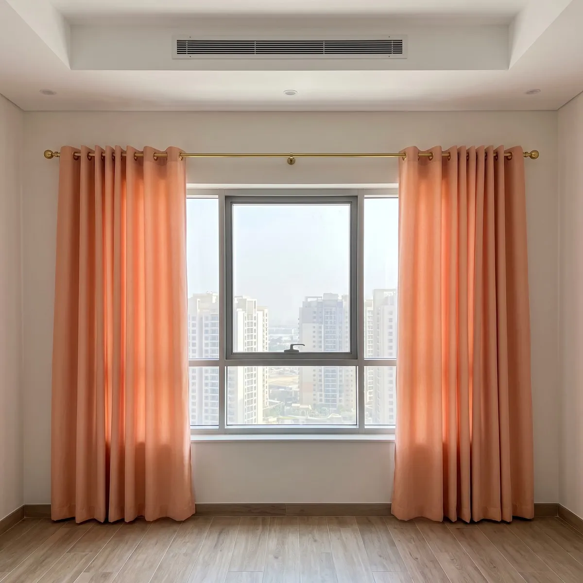 Peach eyelet curtains on a brass pole with a centre bracket, drawn open either side of a window with towers, light glowing in the cloth
