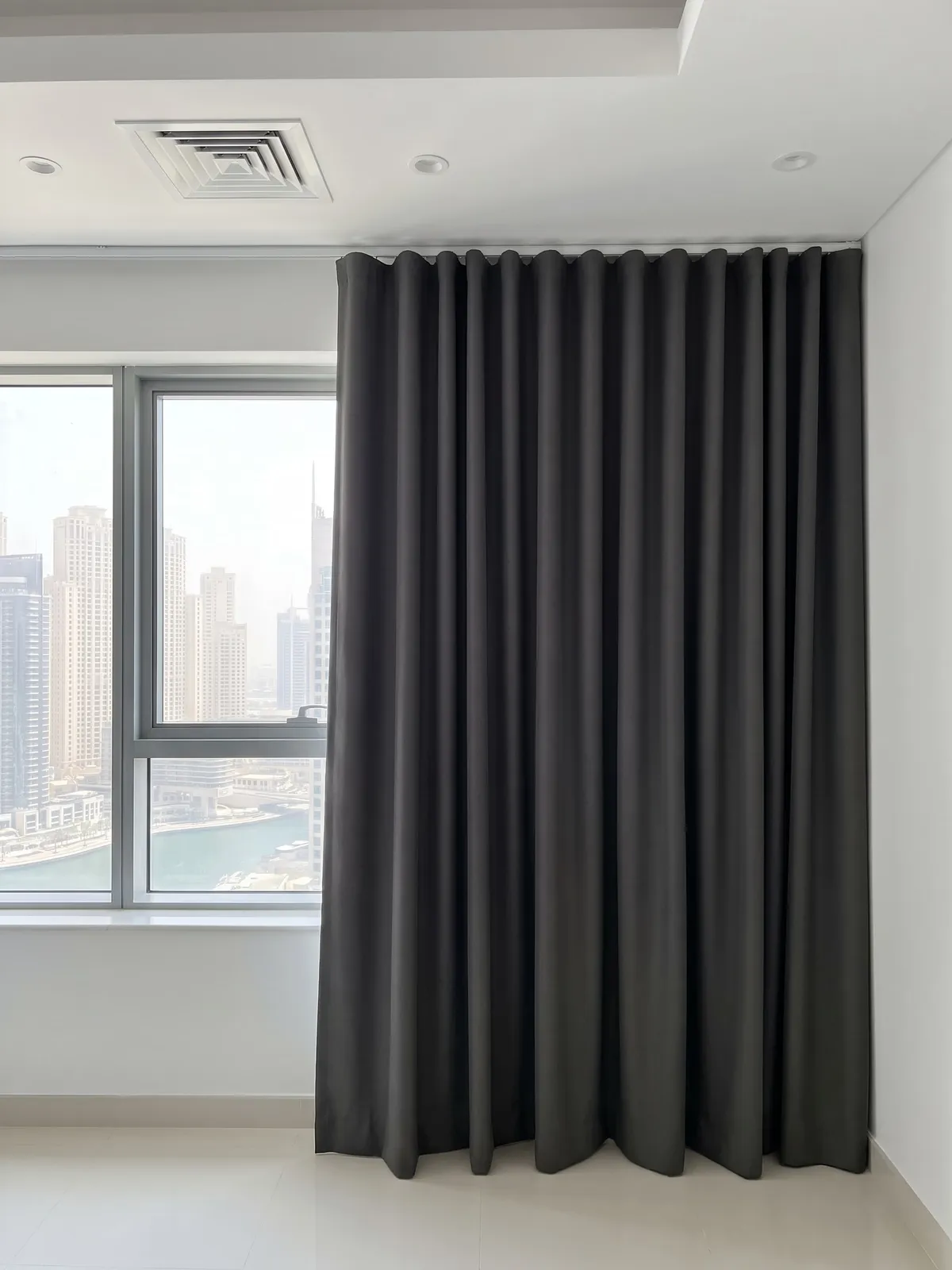 Charcoal heavy curtain with deep folds drawn over the right part of a bedroom window, the marina and towers through the open glass