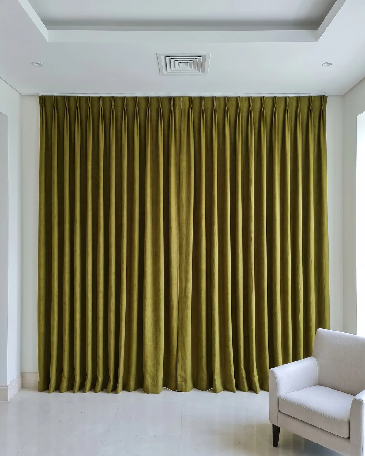 Olive-green linen pinch-pleat curtains closed wall to wall in full folds, no glow through the cloth, a white armchair at right