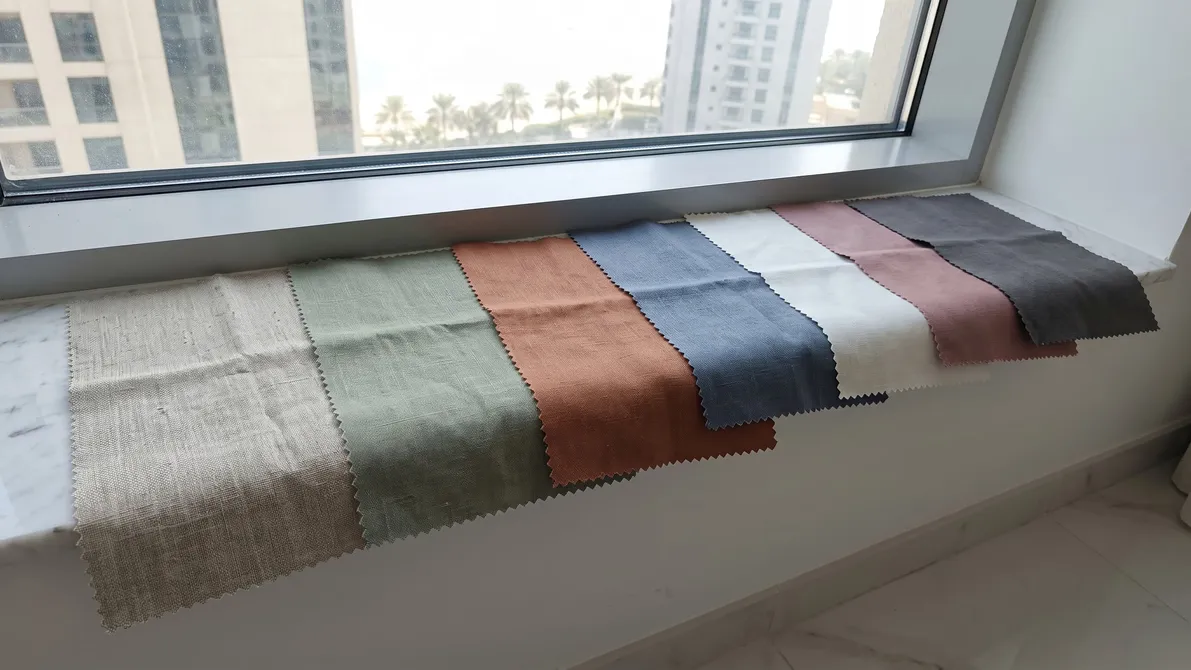 Seven zigzag-edged linen swatches in oatmeal, sage, terracotta, blue, ivory, dusty pink and charcoal along a marble window sill