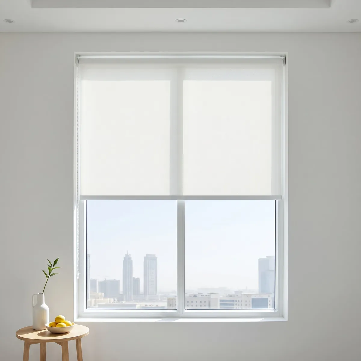 White roller blinds lowered halfway on a window behind a small wooden side table with a white vase and lemons, towers below them