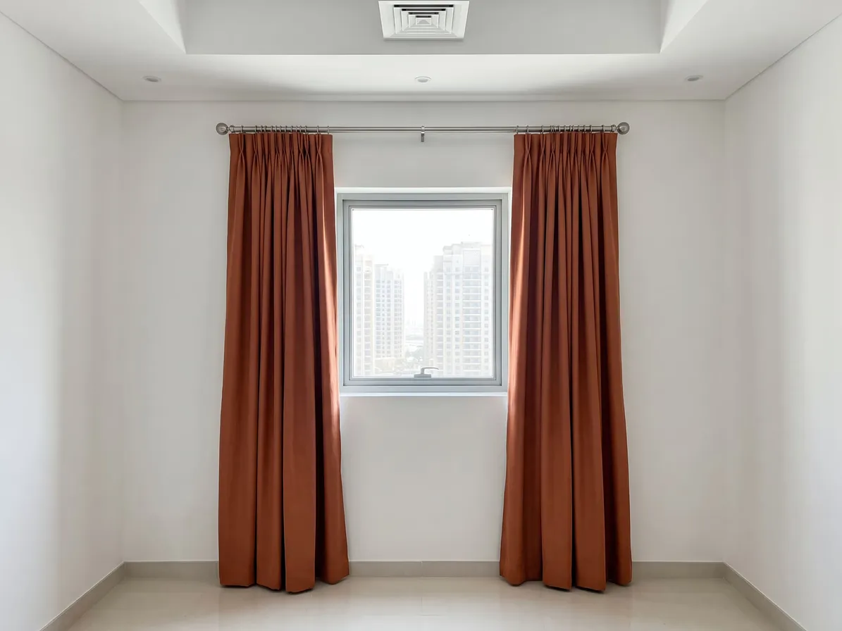 Terracotta pinch pleat curtains on a silver pole with rings, drawn open at both sides of a small window, towers outside