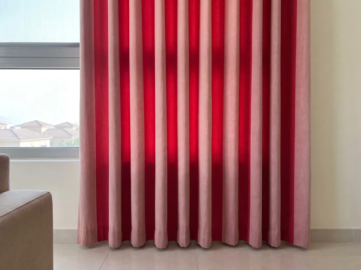 Red curtain with fold faces faded to pale pink stripes and the insides of the folds still bright red, a window with villa roofs at left