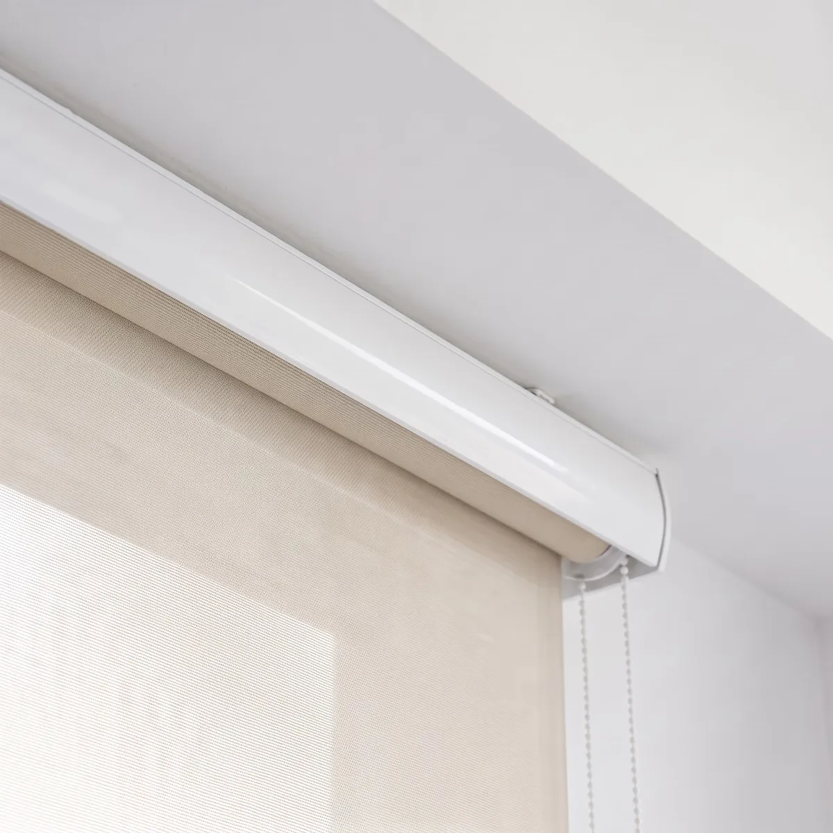 Roller blind seen from below, a white cassette across its top, beige sunscreen fabric beneath it and a bead chain hanging at the right