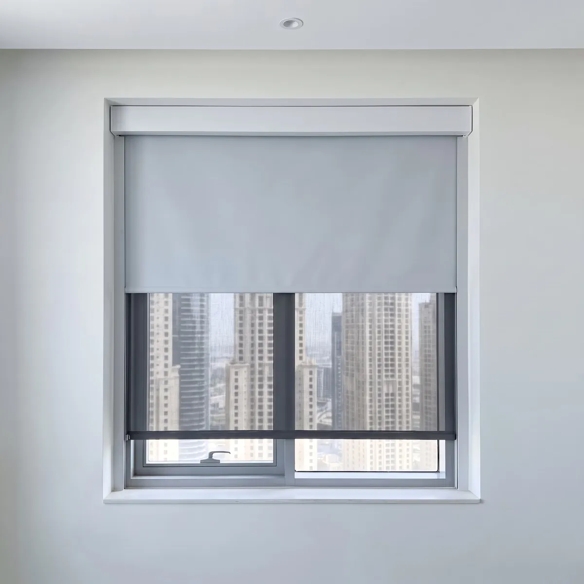 Light grey roller blind half down a window, a charcoal mesh blind lowered further behind it, a white box above, towers seen through the mesh