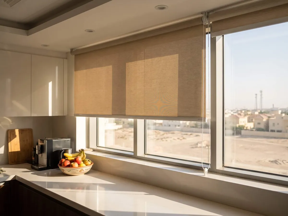 Sand roller blind half lowered over a kitchen window above the counter