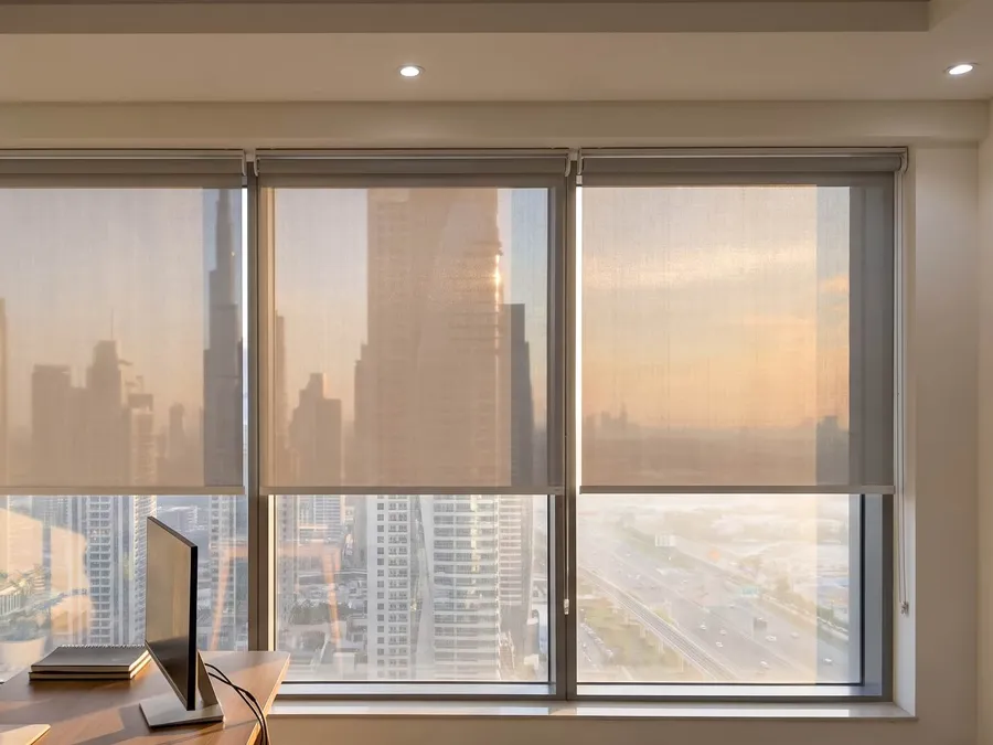 Three sunscreen roller blinds lowered to one line across a wide window