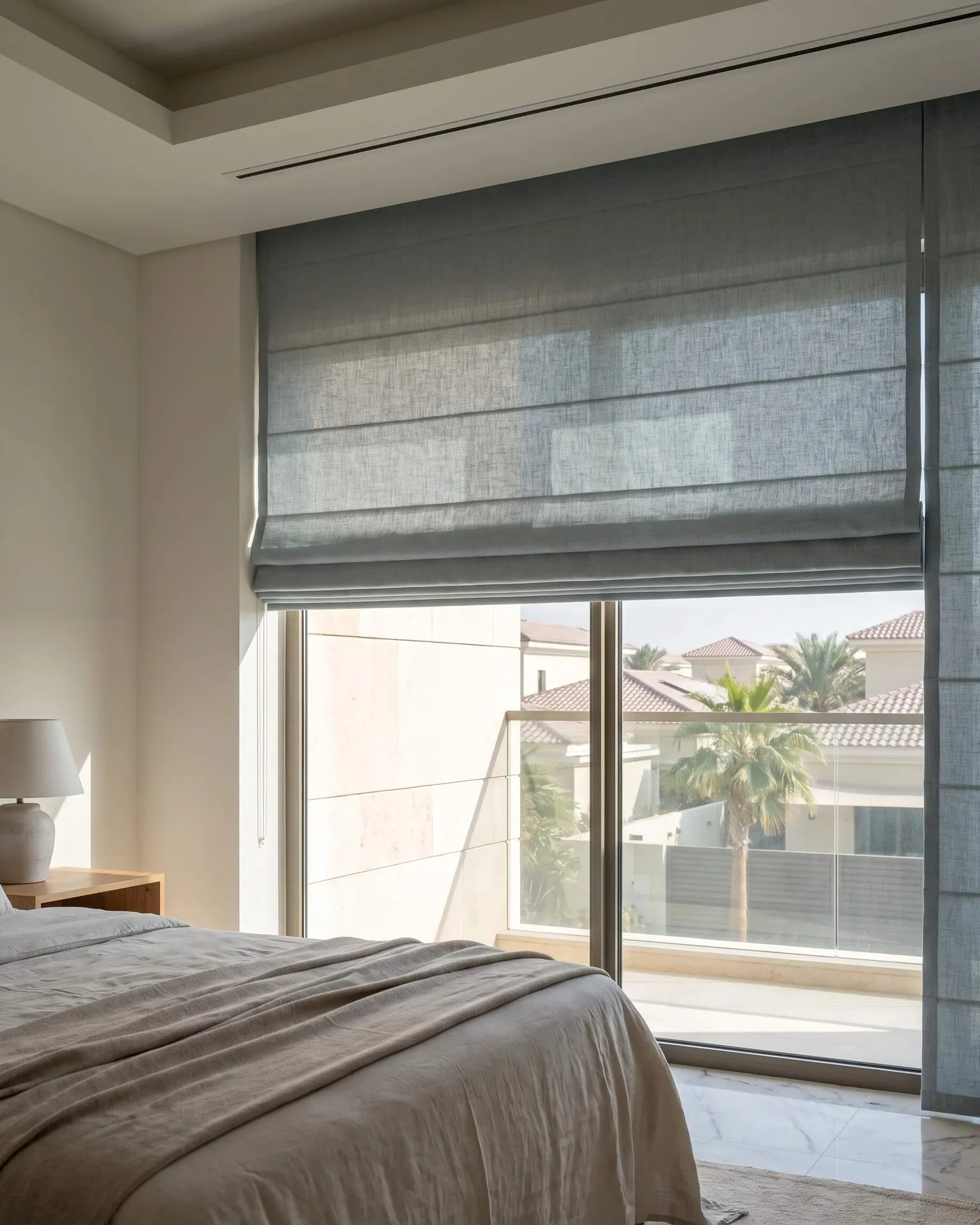 A blue-grey Roman blind half raised over a bedroom window, seen from the foot of the bed