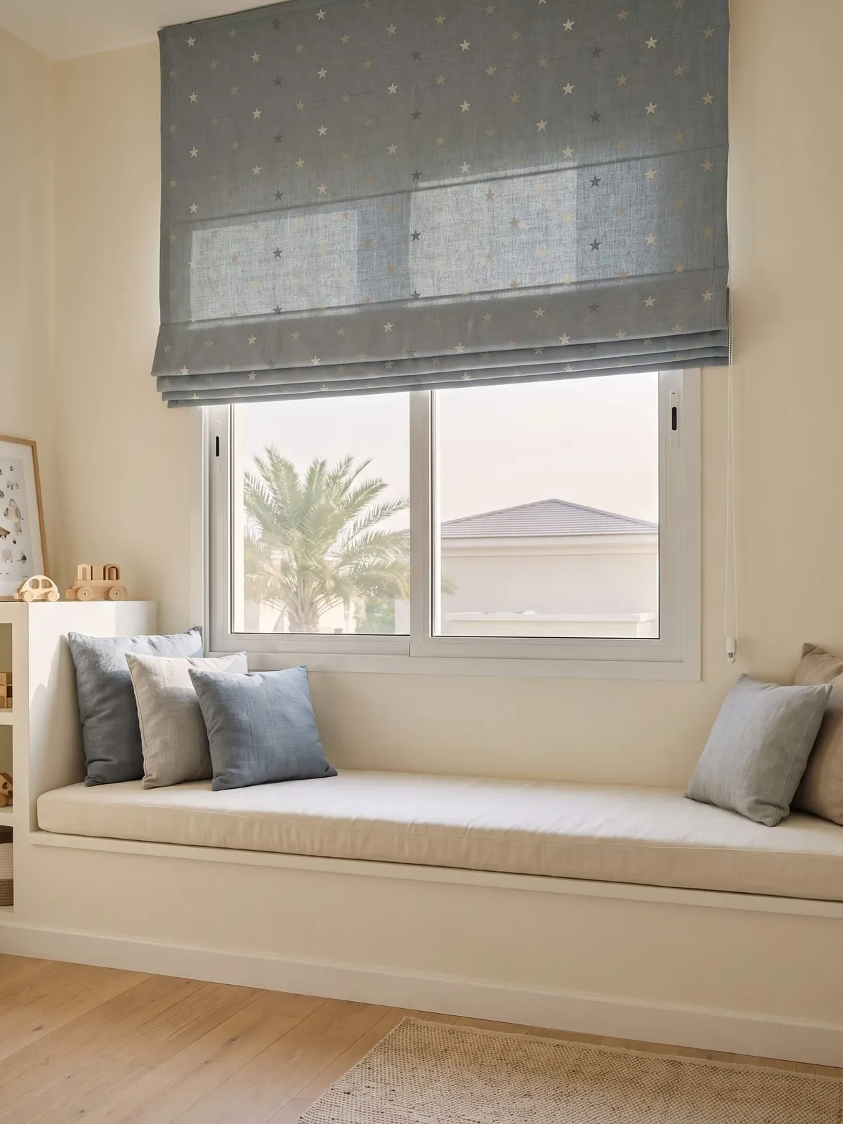 Star-patterned Roman blind half raised over a window seat with cushions in a child's room