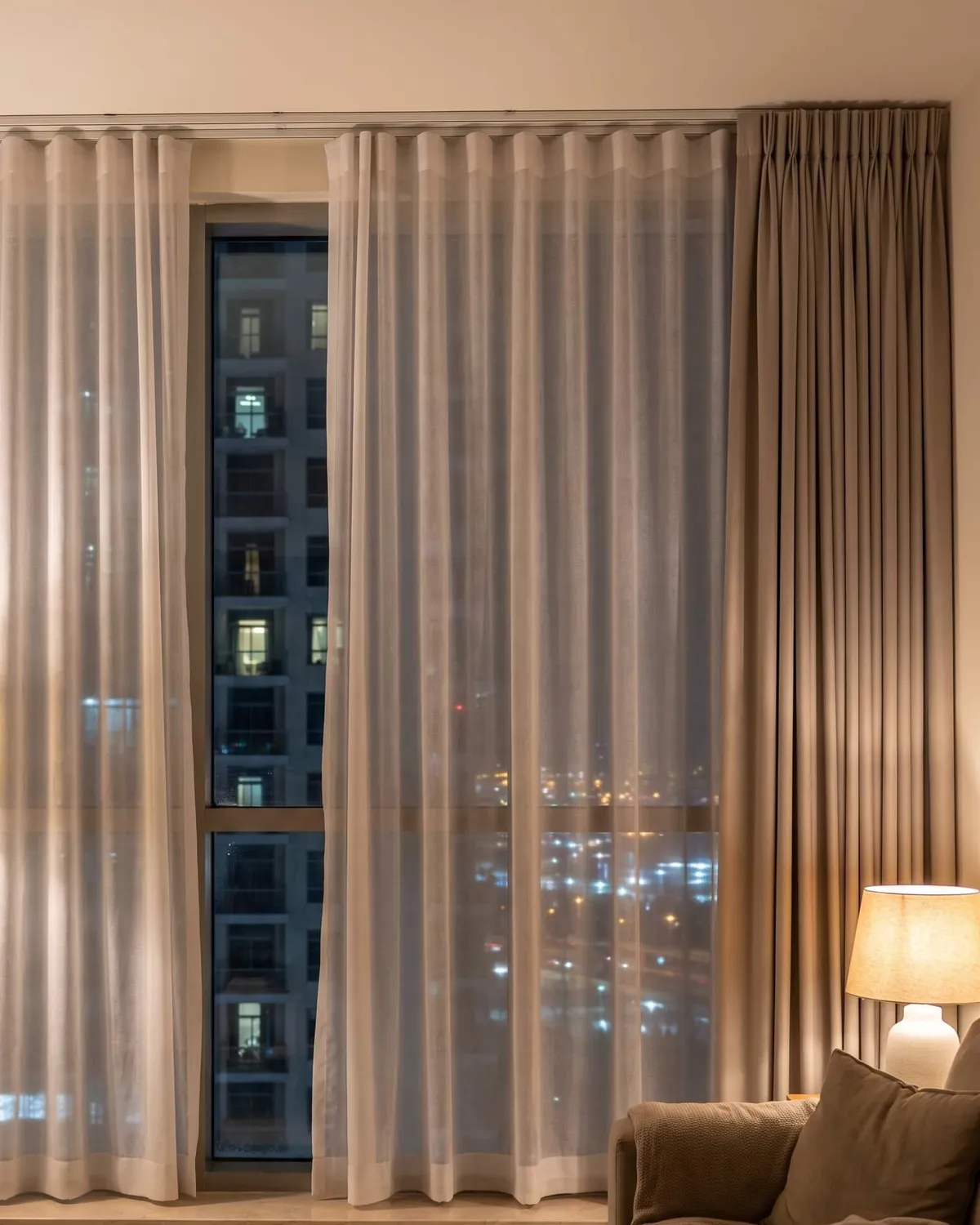 Sheers drawn at night, city lights through them, a lined curtain beside