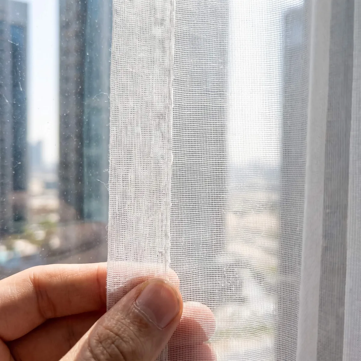 Fine white voile held against a sunlit window, its weave showing