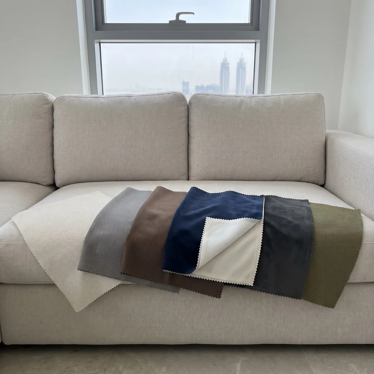 Heavy curtain samples fanned on a pale sofa, ivory, mid grey, mocha brown, navy velvet turned up at a corner, charcoal velvet and olive