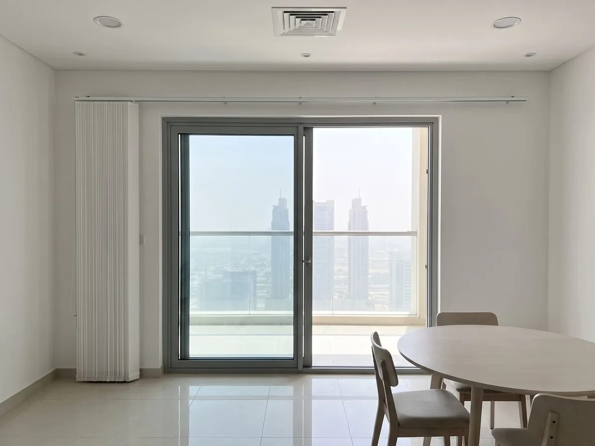 White vertical blind gathered into a narrow stack on the wall beside a sliding balcony door, the glass clear, a round dining table at lower right