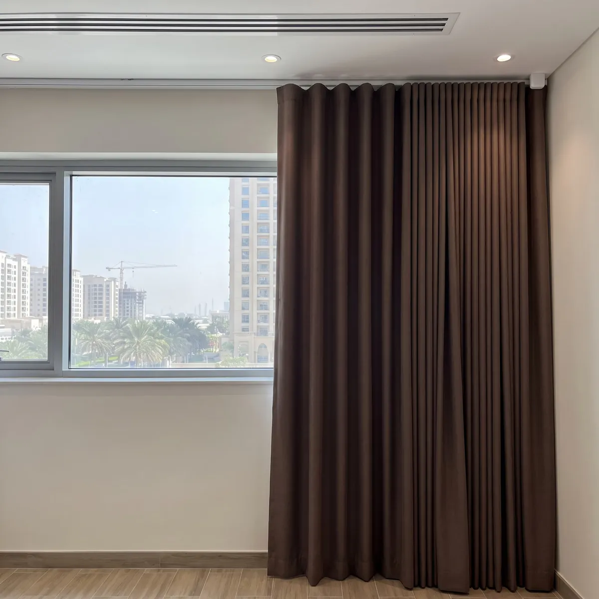 Dark brown wave curtain drawn to the right end of a white ceiling track, a small white box at the track's end, a window at left