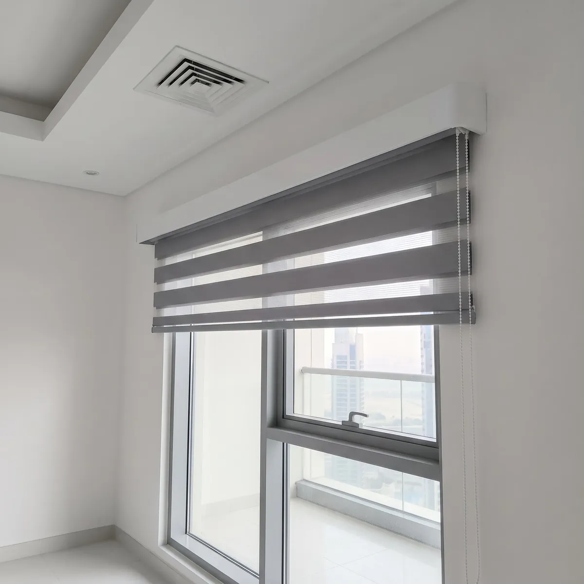 Mid grey zebra blind lowered from a white cassette above a balcony door, seen from below at an angle, towers through the glass